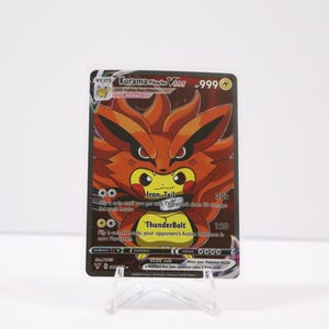 May include: A Pokémon trading card featuring Kurama V, with a fiery orange fox-like creature. The card has the text "Iron Tail" and "Thunderbolt" with a 999 value. The card is displayed on a clear plastic stand.