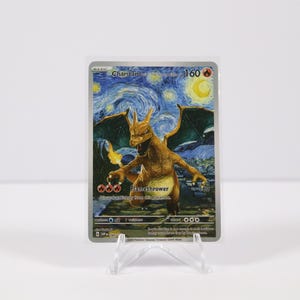 May include: A Charizard Pokémon card with a unique design, featuring a fiery dragon against a starry night sky reminiscent of Van Gogh's style. The card is displayed on a clear stand.