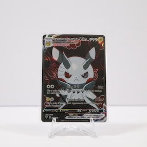 May include: A Pokémon trading card featuring a stylized character with white and gray accents, red eyes, and a stern expression. The card has a black background with red patterns and text, including "Iron Tail" and "Thunderbolt". The card is displayed on a clear plastic stand.