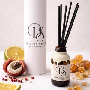 May include: A brown glass diffuser bottle with black reeds and a white wax-like top. A white cylindrical box with the Diffuzor.Studio logo and text is behind the bottle. Sliced lime, lychee, and sugar crystals are scattered around the bottle.