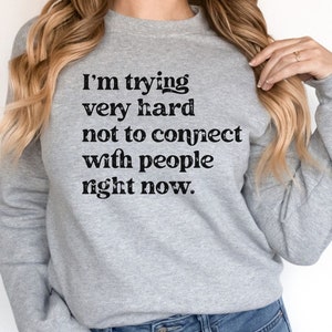 May include: Gray sweatshirt with the text "I'm trying very hard not to connect with people right now." printed in black.