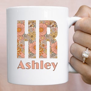 May include: White ceramic mug with a floral design spelling out "HR" and the name "Ashley" below.