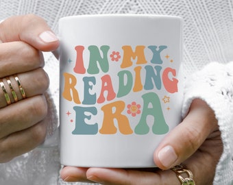 May include: White ceramic mug with the text "IN*MY. READING ERA" in colorful retro font with stars and a flower.