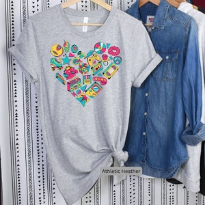 May include: A gray t-shirt with a heart-shaped design made up of various 80s and 90s icons, including a cassette tape, a boombox, a video game controller, and roller skates. The text "Athletic Heather" is printed below the design.