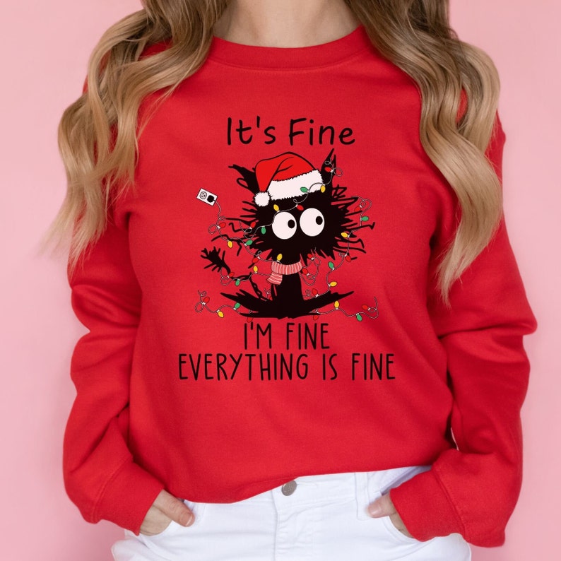May include: Red sweatshirt with a graphic of a black cat wearing a Santa hat and Christmas lights. The text on the sweatshirt reads "It's Fine, I'm Fine, Everything is Fine."