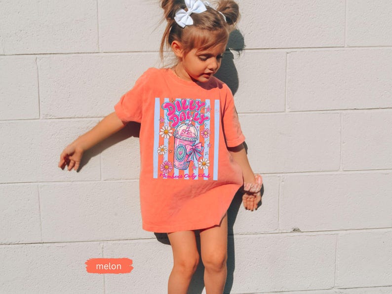 May include: A melon-colored t-shirt with a graphic of a pink drink, daisies, and the text "Silly Daily." The shirt has a vertical striped design in blue and white. The word "melon" is written on a small orange rectangle.