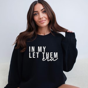 May include: Black sweatshirt with the text "In my let them era" in white lettering.
