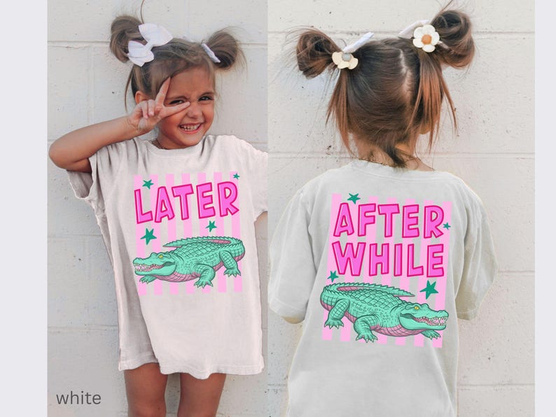 Puede incluir: Camiseta blanca con un dise&ntilde;o de cocodrilo rosa y verde. La parte delantera de la camiseta dice "LATER" en rosa, y la parte trasera dice "AFTER WHILE". La camiseta la lleva un ni&ntilde;o peque&ntilde;o.
