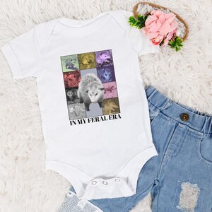 May include: White baby onesie featuring a colourful graphic of opossums and the text "In My Feral Era".
