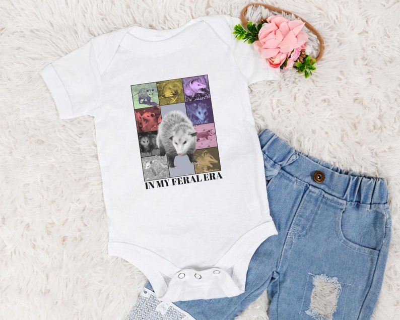 May include: White baby onesie featuring a colourful graphic of opossums and the text "In My Feral Era".