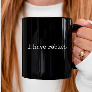 May include: A black coffee mug with the text "i have rabies" in white lettering.