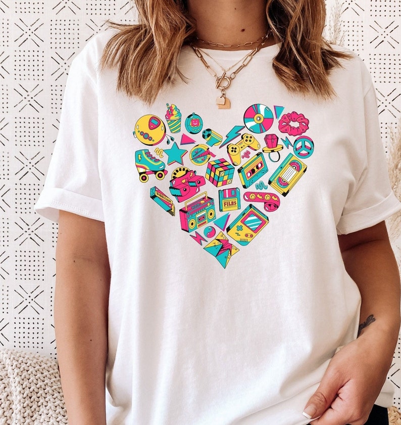 May include: White t-shirt with a heart-shaped design featuring various 80s and 90s icons, including a cassette tape, a boombox, a Rubik's cube, a video game controller, roller skates, a peace sign, a ring, a star, a record, a cassette tape, a film reel, a game cartridge, and a smiley face.
