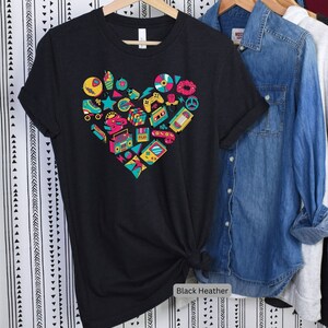 May include: Black heather t-shirt with a heart-shaped design featuring a variety of 80s and 90s icons, including roller skates, cassette tapes, a boombox, a video game controller, and a Rubik's cube.