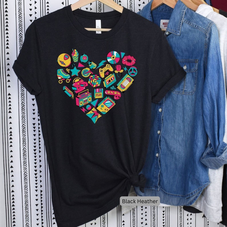 May include: Black heather t-shirt with a heart-shaped design featuring a variety of 80s and 90s icons, including roller skates, cassette tapes, a boombox, a video game controller, and a Rubik's cube.