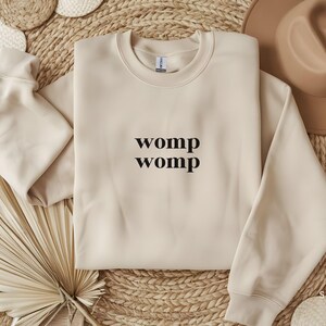 May include: A beige sweatshirt with the text "womp womp" printed in black on the front.