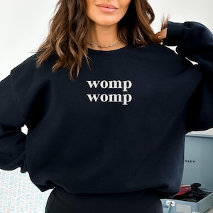 May include: Black sweatshirt with the text "womp womp" printed in white on the front.