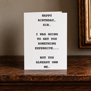 May include: A white greeting card with black typewriter-style text that reads: HAPPY BIRTHDAY, SIR. I WAS GOING TO GET YOU SOMETHING EXPENSIVE... BUT YOU ALREADY OWN ME. The card is standing upright, displaying the message clearly on its front cover.
