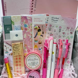 Peut inclure: Un ensemble de papeterie comprenant deux carnets Campus roses, une règle acrylique Lion Gingham Check de 10 cm, deux rouleaux de ruban adhésif, une gomme Sakura Cray-Pas, des autocollants floraux et cinq stylos gel roses et blancs.