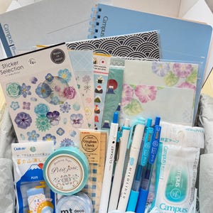 Può includere: Una scatola regalo di cancelleria contenente un quaderno Campus blu, vari fogli di adesivi con disegni floreali e di cibo, due rotoli di nastro adesivo, un righello Gingham Check da 10 cm, una penna Clickart, un pennarello Mildliner, due penne Sarasa e un nastro correttore Campus.