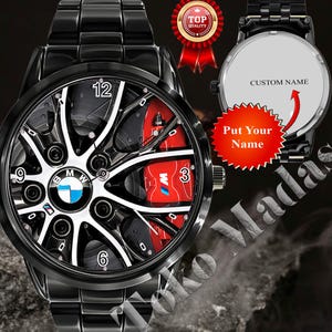 May include: Black wristwatch with a unique design featuring a wheel-like face with the BMW logo, red accents, and the numbers 3, 6, 9, and 12. The watch has a black metal band and the text "Put Your Name" is visible.