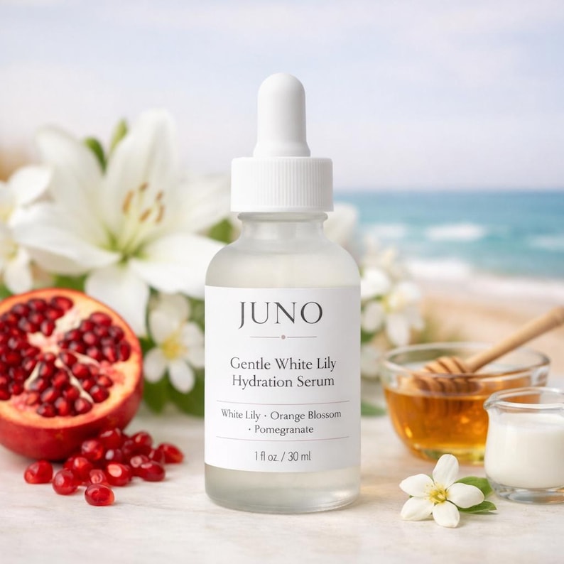 Puede incluir: Una botella de vidrio transparente de "JUNO Gentle White Lily Hydration Serum" con tapa blanca. La etiqueta enumera ingredientes: Lirio blanco, Flor de naranja y Granada. Una granada a la mitad, flores blancas y miel en el fondo. La botella es de 30 ml.