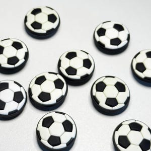 May include: A collection of soccer ball-shaped decorative items. Each item features a classic black and white pentagon design, with a black border. The items are arranged on a white surface.