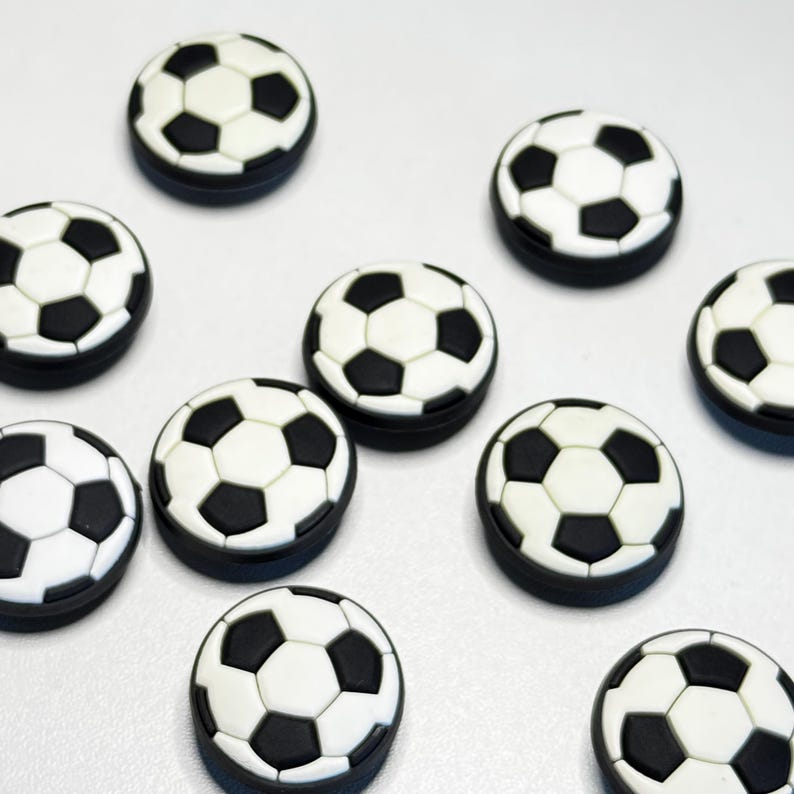 May include: A collection of soccer ball-shaped decorative items. Each item features a classic black and white pentagon design, with a black border. The items are arranged on a white surface.