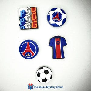 May include: A selection of colourful charms featuring the Paris Saint-Germain (PSG) logo and football-related designs. Includes a football, a jersey, and the Eiffel Tower. The text "Includes a Mystery Charm" is at the bottom.