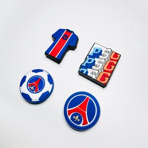 May include: A selection of blue, red, and white Paris Saint-Germain (PSG) themed accessories. Includes a football, a jersey, a logo, and a rectangular piece with "PSG" text. These are likely shoe charms or similar accessories.