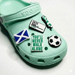 May include: A light green Crocs shoe adorned with decorative charms. Charms include a soccer ball, a Scottish flag, a sign that says "Celtic Park 040 Glasgow", and a charm that says "You'll Never Walk Alone".
