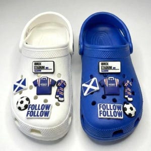 May include: A pair of slip-on clogs, one white and one blue, decorated with football-themed charms including Ibrox Stadium signs, blue jerseys, Scottish flags, scarves, footballs, and rectangular charms with the text Follow Follow.
