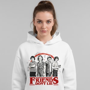 Może przedstawiać: Biała bluza z kapturem z czarno-białą grafiką czterech postaci, z czerwonym okrągłym wzorem i napisem "FRIENDS DON'T LIE" w kolorze czerwonym na dole. Styl casual.