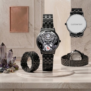 May include: Black watch with a Harley-Davidson skull and engine design on the face. The watch has a black metal band and a matching black ring. Another watch with a blank face and a watch with the back visible are also shown.