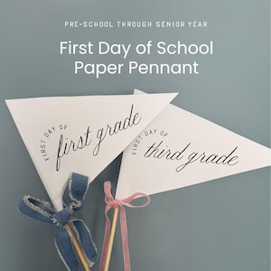 Puede incluir: Dos banderines triangulares de papel blanco sobre palos de madera. Un banderín dice First Day of first grade en letra negra, atado con una cinta de mezclilla azul deshilachada. El otro dice First Day of third grade con una cinta de terciopelo rosa.