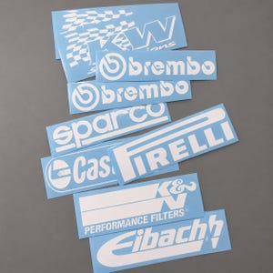 Può includere: Una collezione di adesivi bianchi di marchi automobilistici su carta di supporto azzurra. Gli adesivi presentano i loghi KW, Brembo, Sparco, Pirelli, Castrol, K&N Performance Filters ed Eibach, in vari formati rettangolari e quadrati.