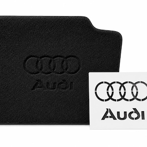 Peut inclure: Tapis de sol de voiture noir avec le logo Audi en relief. Une carte blanche avec le logo et le texte Audi est à côté du tapis.