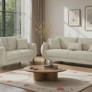 May include: A living room arrangement with a two-seater sofa, a three-seater sofa, and an armchair, all in a light beige fabric. The sofas have curved arms and wooden legs. A round wooden coffee table and a floral rug are also present.