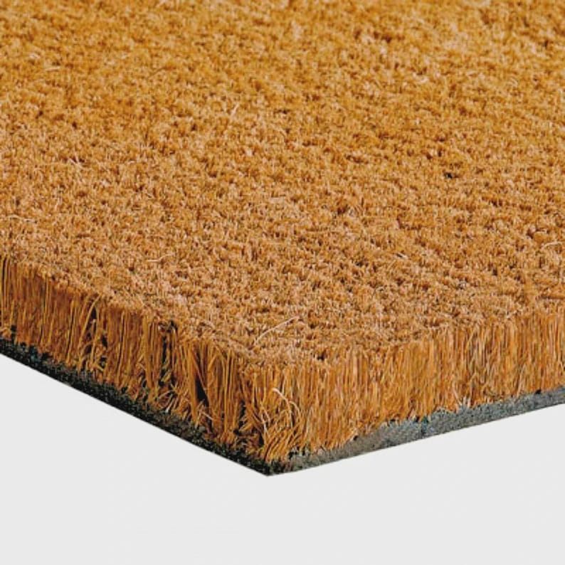 Pu&ograve; includere: Primo piano di un zerbino rettangolare realizzato con fibre di cocco marroni naturali. Il tappeto ha un bordo grigio scuro e una superficie strutturata, ideale per pulire le scarpe. Le fibre sono fitte, creando un accessorio per l'ingresso durevole.
