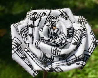 May include: A white fabric rose with a black musical note pattern. The rose is on a brown stem.