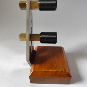 May include: A wooden and metal stand with a rectangular base. The stand has a vertical metal plate with two brass rods and black cylindrical stoppers. The base is made of polished wood.