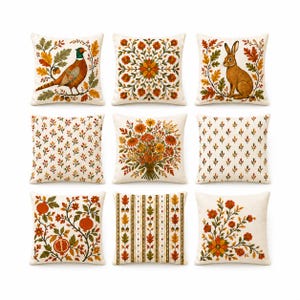 Può includere: Un set di nove cuscini quadrati in tessuto color crema con varie stampe a tema autunnale, tra cui un fagiano, un coniglio, bouquet floreali, rami di melograno, ghiande e motivi geometrici a foglia in tonalità arancione, marrone e verde.