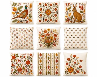 Op de afbeelding: Een set van negen vierkante sierkussens van crèmekleurige stof met diverse herfstthema-prints, waaronder een fazant, een konijn, bloemenboeketten, granaatappeltakken, eikels en geometrische bladpatronen in tinten oranje, bruin en groen.