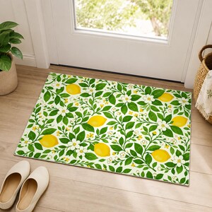 Peut inclure: Tapis de porte rectangulaire avec un motif de citrons et de fleurs. Le motif présente des citrons jaunes vifs, des fleurs blanches et des feuilles vertes sur un fond clair. Le tapis est placé devant une porte blanche.