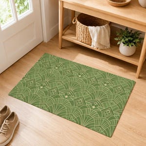 May include: A rectangular green and beige patterned rug. The rug features a repeating geometric design of fan-like shapes and squares. The rug is placed on a wooden floor near a door and a wooden console table.