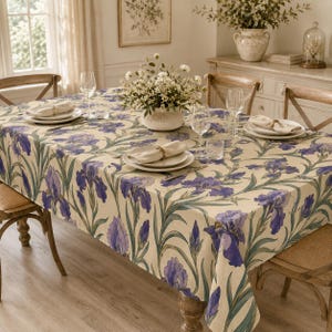 May include: A rectangular tablecloth featuring a repeating pattern of purple iris flowers with green stems and leaves on a cream background. The tablecloth is draped over a wooden dining table set with white plates, clear glasses, and a floral centerpiece.