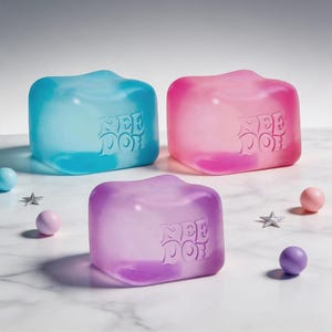 May include: Three translucent, cube-shaped objects in blue, pink, and purple, each with the word "NEE DOR" embossed on the front. The objects are surrounded by small, round, pastel-colored spheres and star-shaped decorations on a marble surface.
