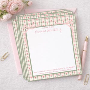 Puede incluir: Papelería personalizada con un diseño de cuadros de flores rosas y verdes. La papelería presenta el texto "a note from Canaan Martinez" y una cita de Proverbios 31:25. También se ven un sobre, un bolígrafo y un clip rosas.
