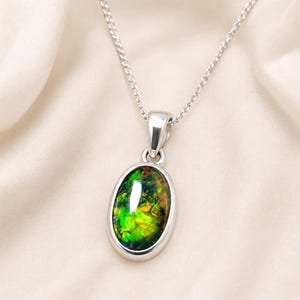 May include: A silver pendant necklace featuring an oval-shaped stone with a dark base and vibrant, iridescent flashes of green, yellow, and orange. The stone is set in a smooth, polished silver bezel and hangs from a delicate silver chain.