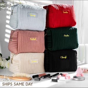 Könnte beinhalten: Ein Stapel von sechs personalisierten Kosmetiktaschen in verschiedenen Farben: Hellblau, Rot, Dunkelgrün, Rosa, Creme und Schwarz. Jede Tasche hat einen goldenen Reißverschluss und einen goldgestickten Namen. Die Taschen sind aus geripptem, plüschigem Material. Der Text "SHIPS SAME DAY" steht unten.