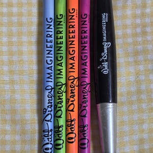 Könnte beinhalten: Eine Sammlung farbiger Bleistifte und ein schwarzer Marker. Die Bleistifte sind in Blau, Grün, Orange und Lila gehalten, jeder mit dem Aufdruck "Walt Disney IMAGINEERING". Der schwarze Marker trägt ebenfalls das Logo "Walt Disney IMAGINEERING".